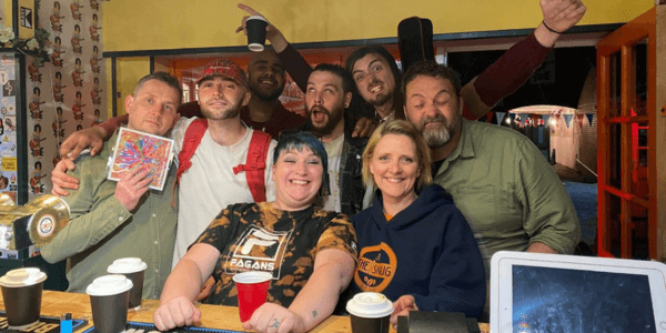 All the team members of the snug coffee house and the band The Pagans smiling at the camera behind the counter.