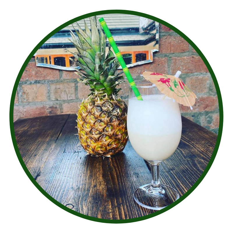 Image shows a Snug Tropicana cocktail with a straw beside a pineapple