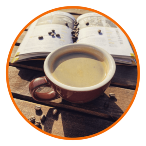 image shows a coffee along side an open book with some loose coffee beans down the centre