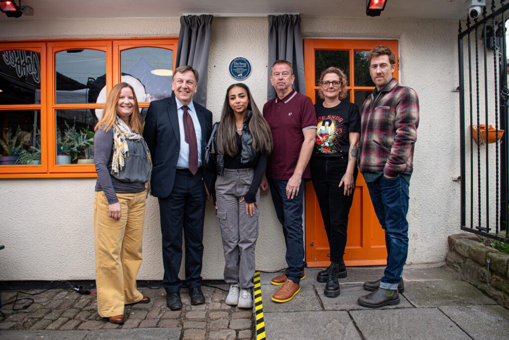 Claire Mera Nelson, John Whittingdale MP, Jennifer King singer songwriter, Mark Davyd from the MVT and Rachael Flaszczak and Jamie Lawson stood in front of the Music Venue Properties Plaque on the wall at The Snug Coffee House in Atherton.