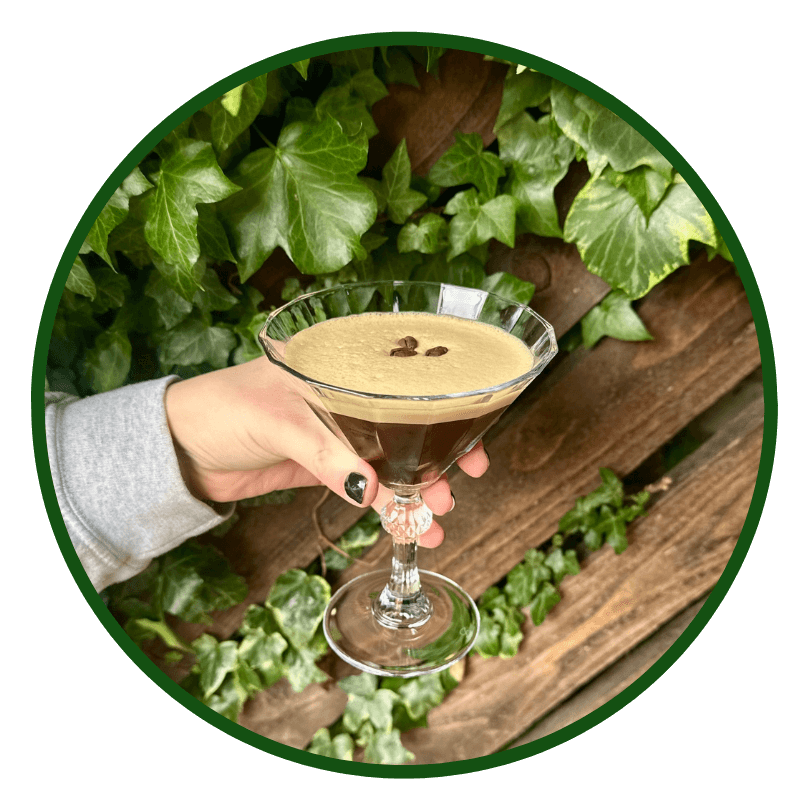 A person holding up a martini in front of ivy