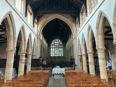 Interior of St Chad’s Church in Rochdale, showing rows of seating, stone arches and the altar beneath a large stained glass window.